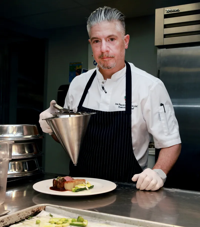 Maître Rôtisseur Joe Piazza in the kitchen with a sauce funnel
