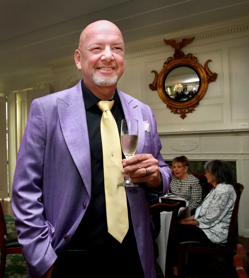 Member in a purple jacket and gold tie with champagne in hand