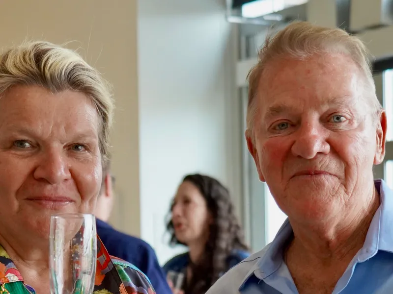 A member in her medal collar toasting champagne with a guest
