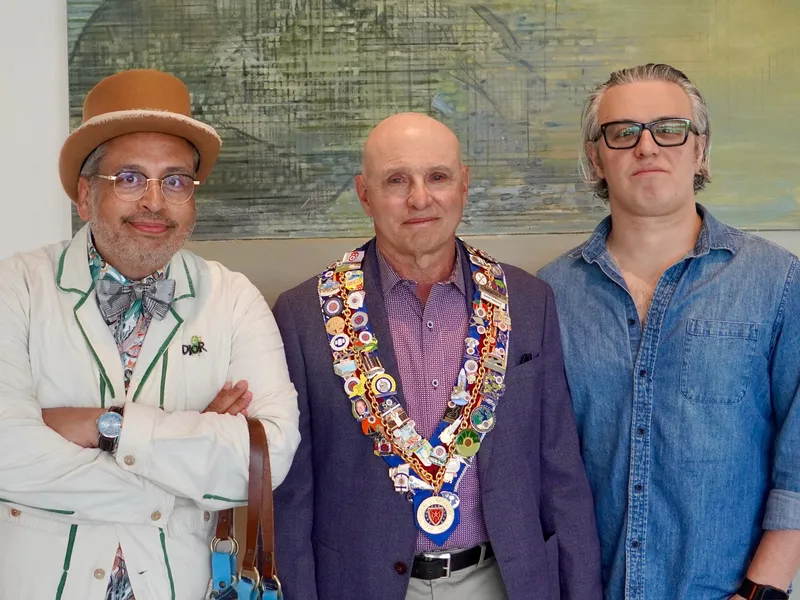 Three members before a painting, one in a medal-covered collar